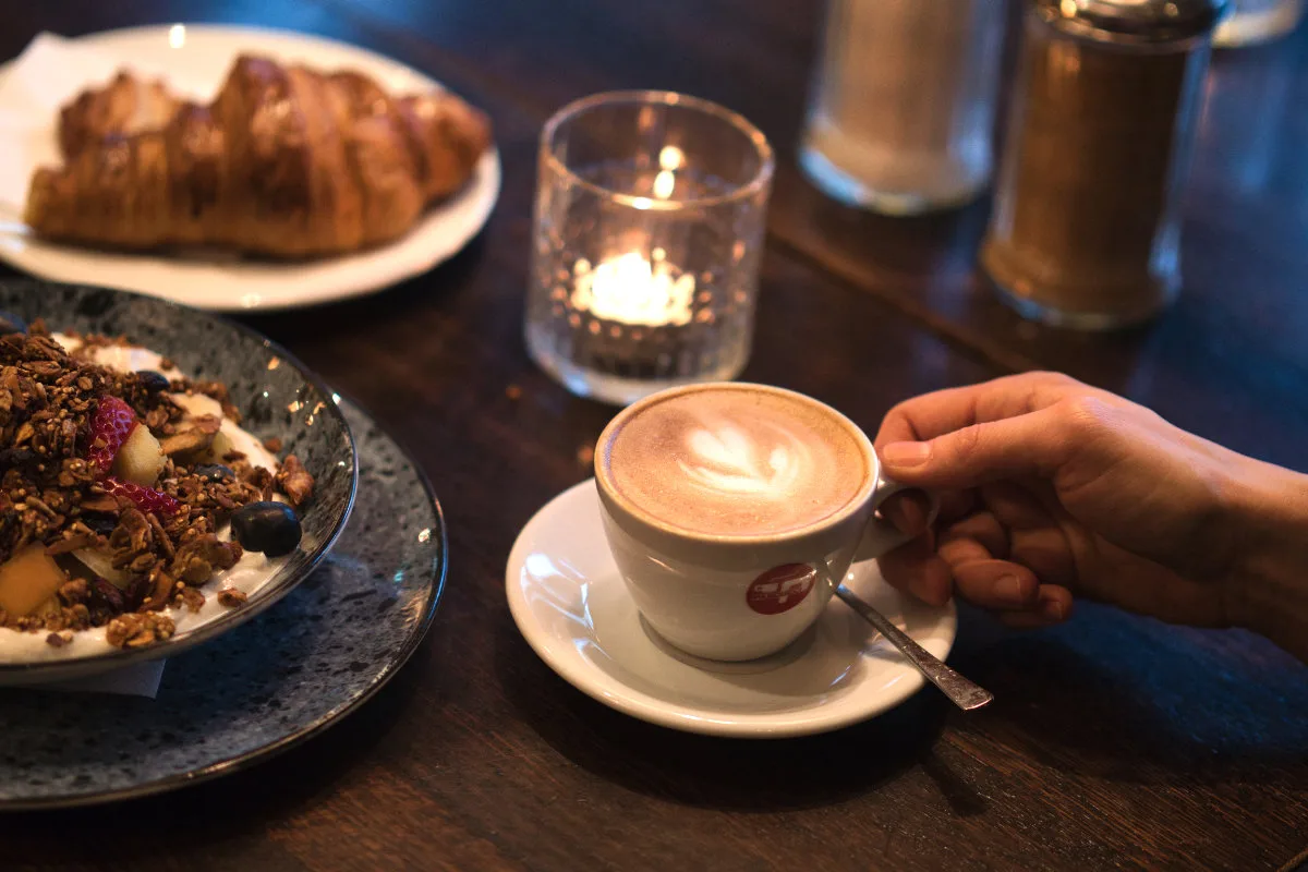 Foodfotografie im Café: Cappuccino, Croissant und Frühstücksteller auf dem Holztisch